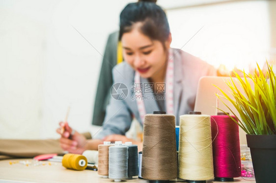 商业与模糊快乐的女裁缝和衣服装设计师背景搭配的彩色线接合在车间办公室制作新的收藏品人民生活方式和自由职业工作妇女时尚缝纫图片