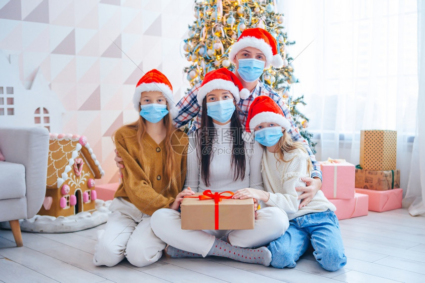 来源四口圣诞快乐家庭节上送礼物的四口之家父母和孩子都戴着面纱年轻家庭快乐孩子们拿着圣诞礼物的孩子女健康图片