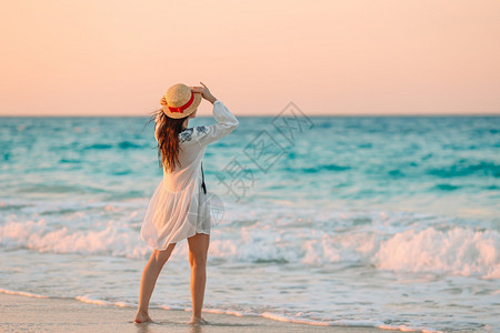 闲暇水在日落的热带海滩上年轻的美丽女人在黄昏的热带海滩上年轻漂亮的女孩在美丽着装背景的年轻女孩后视中黑发图片