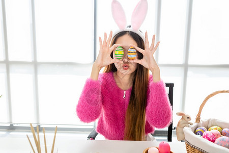 庆典春天家庭带着兔子耳朵的亚洲年轻女子当着她的眼在白色房间背景中扭曲时在她眼前举起一个多彩的复活节鸡蛋图片