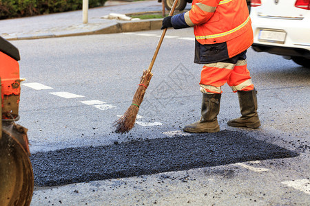 出去道路施工人员在修好的路段上用木头水平整新鲜沥青筑路工人在部分道上收集新鲜沥青并将其平整以便在道路施工中进行维修等级构造图片