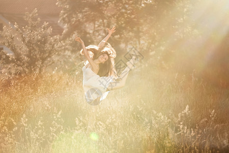女士芭蕾舞者在草地上做阿拉伯礼仪穿着白裙子在自然背景和日落的光芒中户外艺术图片