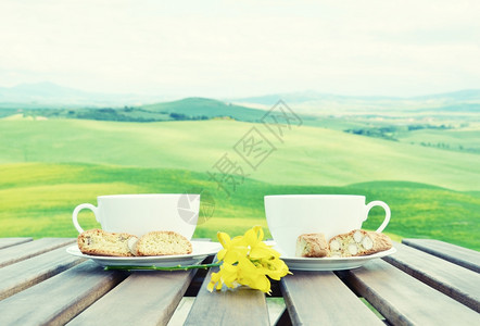 木制桌子上两个咖啡杯和罐头的过滤图像意大利托斯卡纳风景方格的意大利语早餐图片
