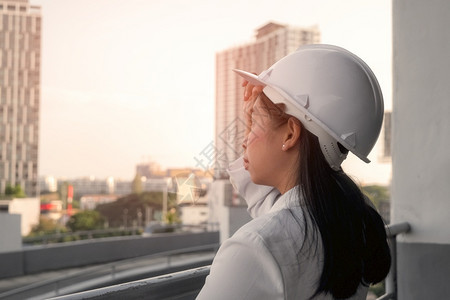 在建筑工地带平板电脑的女建筑工程师戴着白色头盔的自信女建筑师看着工地和概念商业环境职图片