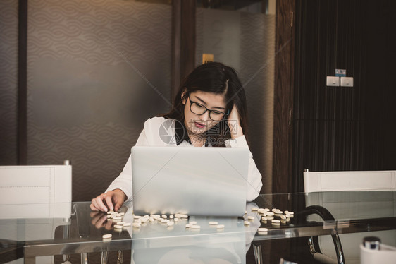 生病的亚洲萧条女商人在从事计算机笔记本电脑工作的同时还从事业余行动在现代会议室办公服药商业生活方式和压抑概念等亚洲低迷的商业妇女图片