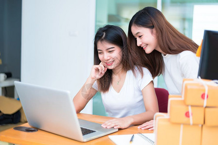 女顾客两名年轻的自由职业青年亚洲女企家在庭办公室用笔记本电脑或计算机笔记本和桌上包装提供在线购物和营销服务向客户提供书桌包装的笔图片