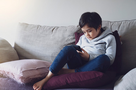自己活动深的孩子用手机自我隔离做作业悲伤的孩子坐在沙发上低头沉思男孩在家上学期间网习在线教育图片