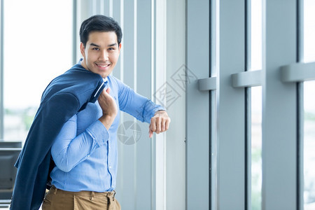 一个快乐成功的感觉肖像赢者英俊年轻的亚洲青商人穿着一件蓝外套的人商服和在窗户上的蓝衬衫在办公室背景里微笑行政人员们图片