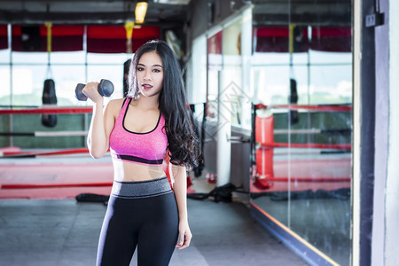 强的黑发重量亚洲女在体育健身室内运动和俱乐部中进行有哑铃运动的锻练训并配有运动设备体操背景的健身俱乐部亚裔妇女图片