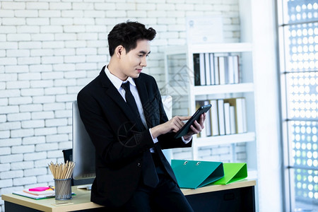 独自的灰色一位愉快乐心情一个成功的亚洲青年商人在办公室用智能手机和笔记本电脑做木制桌底背景工作保持图片