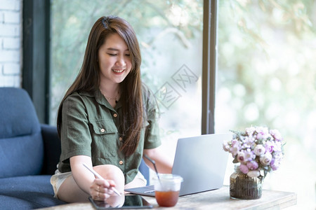 互联网在数字平板电脑和膝上型计算机电子笔咖啡杯如背景通信概念等在咖啡店的杯上作笔记的工妇女临时注意到以电子笔和制作的数字平板电脑图片