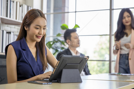 讨论快乐的商业妇女使用现代数字平板电脑而同事在办公室团队工作会议和伙伴关系概念的背景中进行互动女商人使用现代数字片公司图片