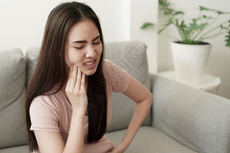 衰变病人敏感的亚洲妇女在家里坐沙发上时有牙痛亚洲女孩脸上的表情达方式是牙痛和科药物亚洲妇女有牙痛图片