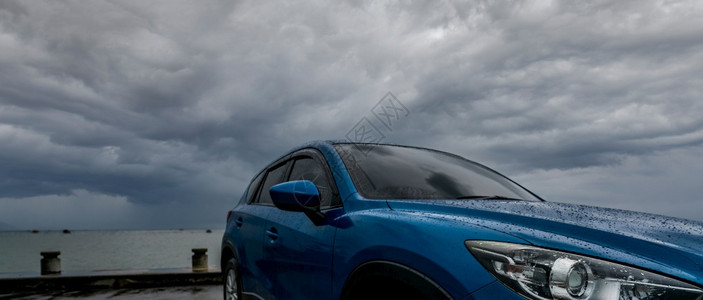 洗放松蓝色SUV车上有水滴停在海滨附近的车场与暴风雨和阴云的天空抗风暴和云对前线看到新的豪华SUV车并设计体育在雨季驾驶汽车夜晚图片