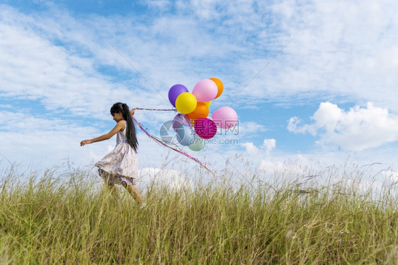 快乐的可爱女孩拿着气球在绿色草地白云和蓝天空上运行快乐的天空手拿着充满活力的空气球在生日派对上玩欢乐的可爱女孩明亮束跑图片