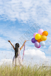 快乐的可爱女孩拿着气球在绿色草地白云和蓝天空上运行快乐的天空手拿着充满活力的空气球在生日派对上玩欢乐的可爱女孩愉快保持士图片