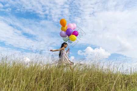 太阳快乐的可爱女孩拿着气球在绿色草地白云和蓝天空上运行快乐的天空手拿着充满活力的空气球在生日派对上玩欢乐的可爱女孩子图片