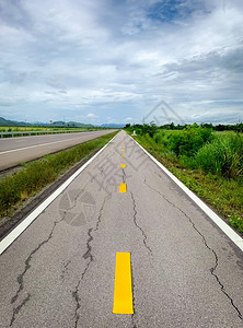 黄色的通往山顶沥青道路长直线损坏的沥青道路自然景观边空旷自行车道和白天空及满有绿草的云层户外白色图片