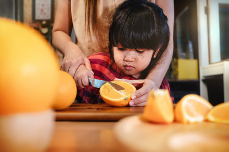 厨房喜悦快乐的可爱34岁年老女孩与她的妈切除一些橙子在木质餐桌上食品室的青春女孩正在学习烹饪她的母亲水果和蔬菜的孩子概念肖像图片