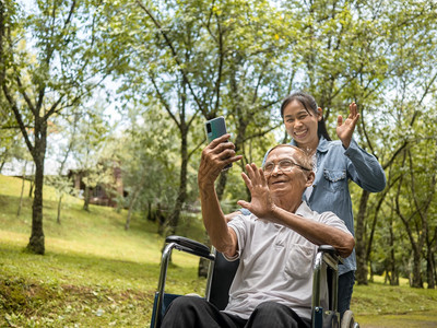 推动女坐在轮椅上的祖父和孙女通过智能手机与亲戚交谈视频电话在公园里过着度假的家庭生活亚洲人图片