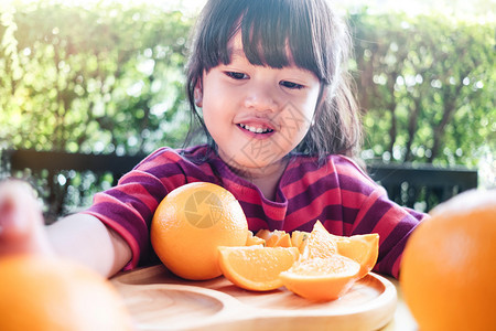 微笑果子和儿童蔬菜夏天34岁女孩在木制花牌新鲜果汁水上吃着橙子的小可爱34岁女孩概念为了快乐的图片
