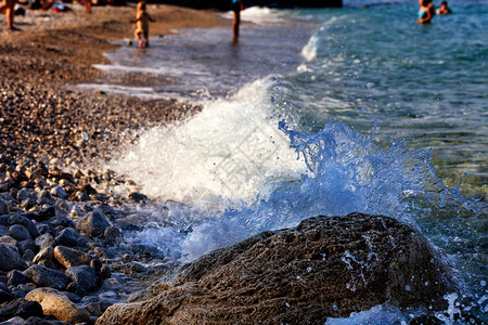 海景冲浪在滨大块巨石上冷冻的海浪喷洒其背景是人们在海边大块巨石上沉卧在模糊的海浪波中晚上图片