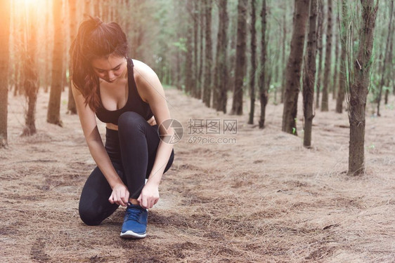 她的运动女人在森林里慢跑时绑起鞋带着饮用水瓶回到森林边上妇女们用自来水瓶把人和生活方式概念捆绑在一起保健和福利主题公园和户外主题图片