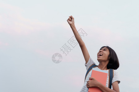 旅行亚洲女学生成功快乐面露兴奋同时在夏天早上拿着一本手举起的书到蓝天背景夏日清晨愉快瞳孔图片