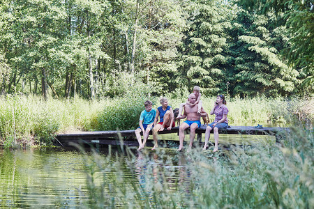 绿化家庭一起花时间坐在湖边的桥上与自然相近的树木之间在暑假期Candid人真实时刻情况中叶子女士图片