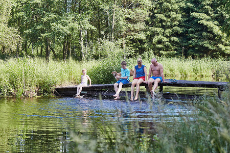 人们放松生长家庭一起花时间坐在湖边的桥上与自然相近的树木之间在暑假期Candid人真实时刻情况中图片