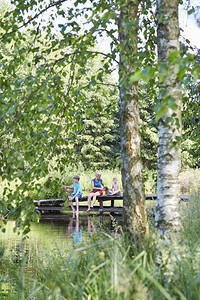 绿化家庭一起花时间坐在湖边的桥上与自然相近的树木之间在暑假期Candid人真实时刻情况中绿色正的图片