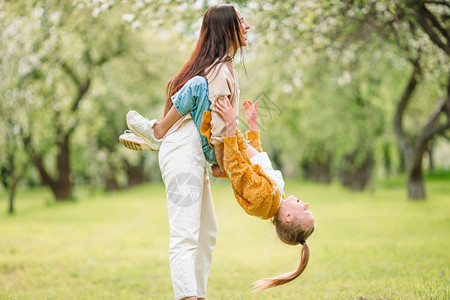 母亲和女儿的家庭在公园户外玩得开心在盛的樱花园中母亲和女儿家庭父母女孩樱桃图片