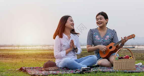 年轻的笑午餐一群亚洲朋友玩UkeleleUkelele并花时间在暑假野餐他们快乐节假日愉图片