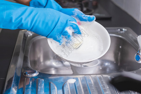 盘子工作一个穿着蓝色橡胶手套的近身男子在厨房水槽里用洗碗液杯子他当时正戴着一个蓝色橡胶手套关心图片