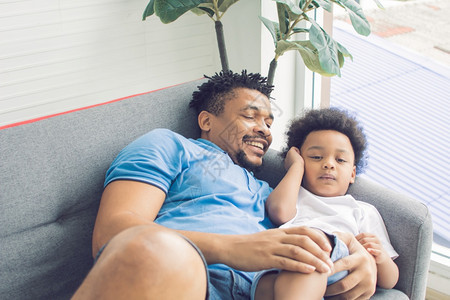 爸学龄前儿童自己的非洲黑人父亲正在家庭教育和概念的起居室与儿子睡觉和玩耍儿童教育和家庭概念图片