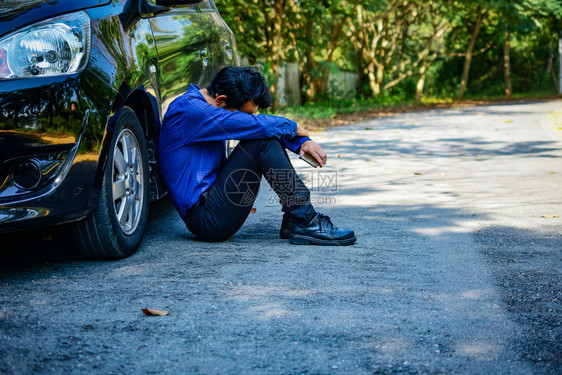 路线损害赔偿持智能电话和坐在停路边的汽车上失望男子图片