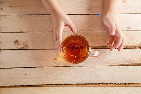 品尝保持健康儿童用手握着透明的茶杯在浅木背景上举着茶杯图片