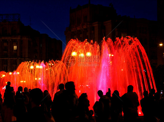 深夜喷泉周围人群的黑暗剪影红色霓虹灯照亮了强大的城市歌唱喷泉流红色霓虹灯照亮了深夜强大的城市歌唱喷泉流闲暇城市蓝色图片
