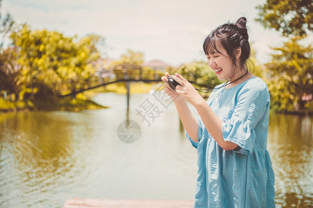视频公园里身穿蓝色连衣裙的亚洲女手持数码无反光镜相机不戴口罩拍照心情愉快人们的生活方式和休闲概念户外旅行和自然主题服用女士图片