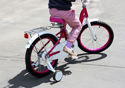 健康女孩骑着粉红子的自行车在铺路面上孩子们铺砌图片