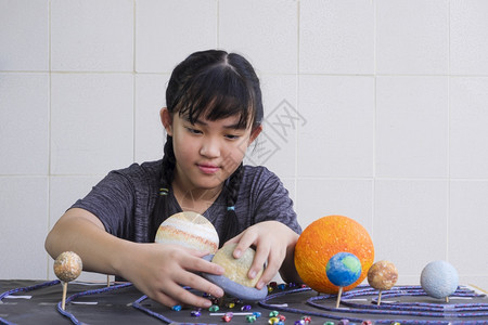 基本的海王星选择地关注亚洲年轻女孩在学校科家庭项目中在里木板桌上自制太阳系模型的自制太阳系模型以便有选择地关注这些年轻的亚洲女孩图片