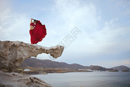 女身穿红礼服的黑发年轻女人在海滨附近岩石上跳舞多于赤脚图片