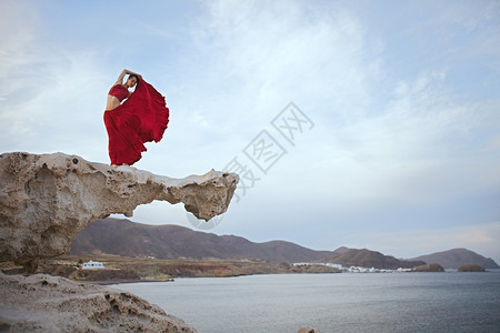 卵石身穿红礼服的黑发年轻女人在海滨附近岩石上跳舞水平的戏服图片