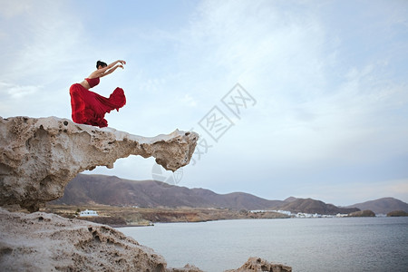 舞蹈纺织品水平的身穿红礼服黑发年轻女人在海滨附近岩石上跳舞图片