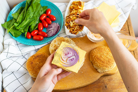 躺着准备制作汉堡的所有配料小圆面包炸肉排奶酪沙拉番茄酱汁顶视图girlrsquos的手拿着汉堡小圆面包放在紫色蝴蝶结上准备制作汉图片