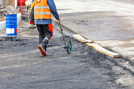 一名测量公路距离的工程师用一个计量轮确定铺在公路新段设所需沥青量A道路工程师使用电子计量轮测工作站点A道路工程师使用电子计量轮测图片