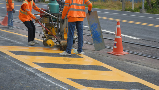 交通安全路面有反射背心和热塑料喷雾路标记机器的公路工人正在努力为沥青路上的交通黄线涂漆铁路横穿街道表面选择地聚焦于道路通讯团体热塑料背景