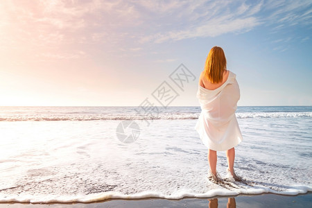 水红头发的嫩女孩赤脚站在海滩上的白色冲浪泡沫中穿着白色连衣裙的女人在海边阳光明媚的早晨红头发嫩女孩赤脚站在海滩上的白色冲浪泡沫中图片