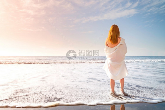 水红头发的嫩女孩赤脚站在海滩上的白色冲浪泡沫中穿着白色连衣裙的女人在海边阳光明媚的早晨红头发嫩女孩赤脚站在海滩上的白色冲浪泡沫中图片