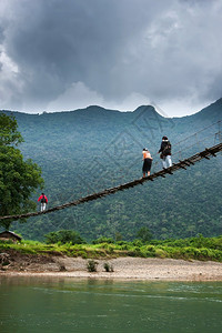 学校超过风暴一群老挝高中女生穿过南宋河上简单的悬吊脚桥在北老挝农村背景的山上云雾笼罩着巨大黑暗位于北老挝农村地区图片